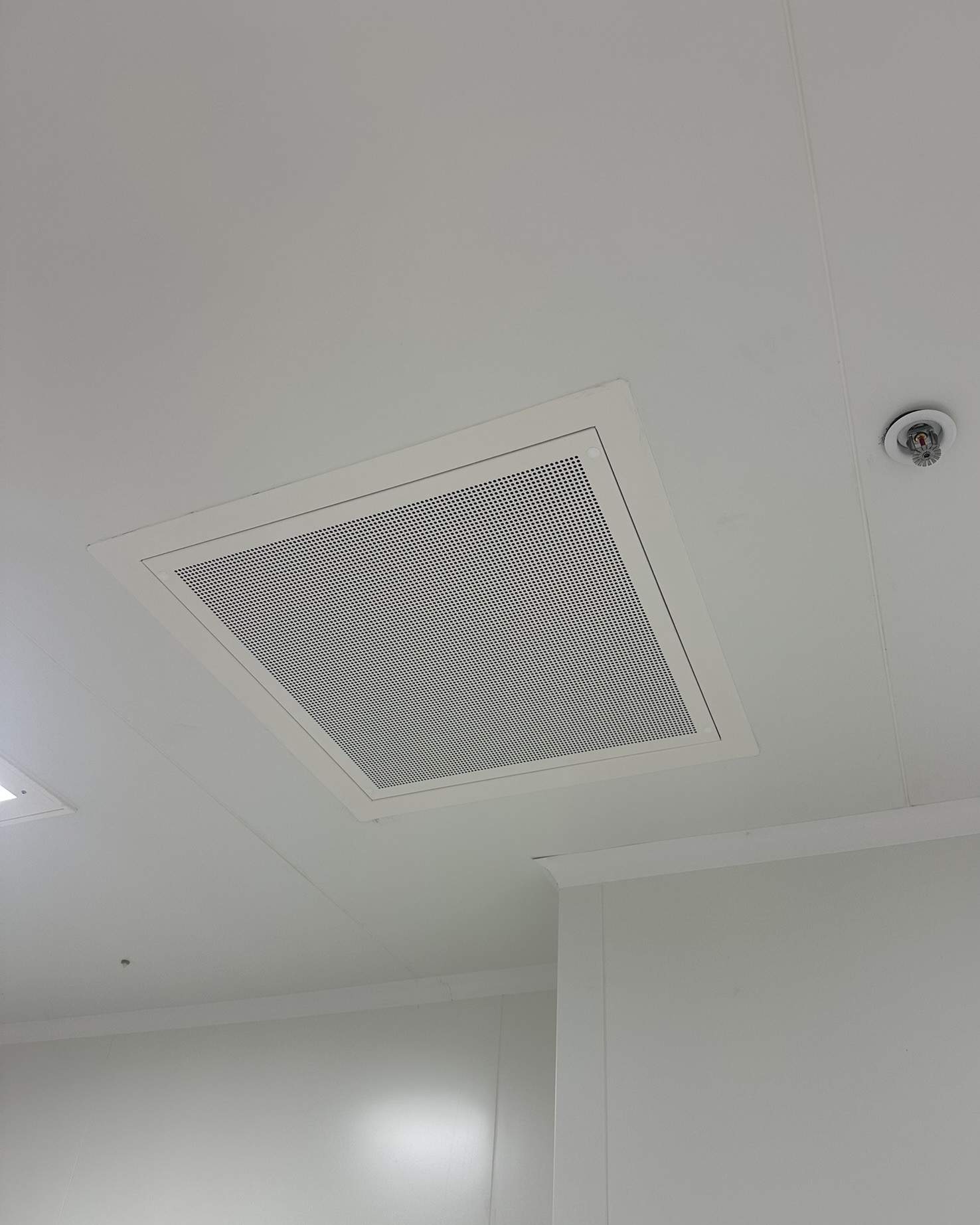 Diffuseur d'air perforé installé au plafond d'une salle propre, à proximité d'un sprinkler