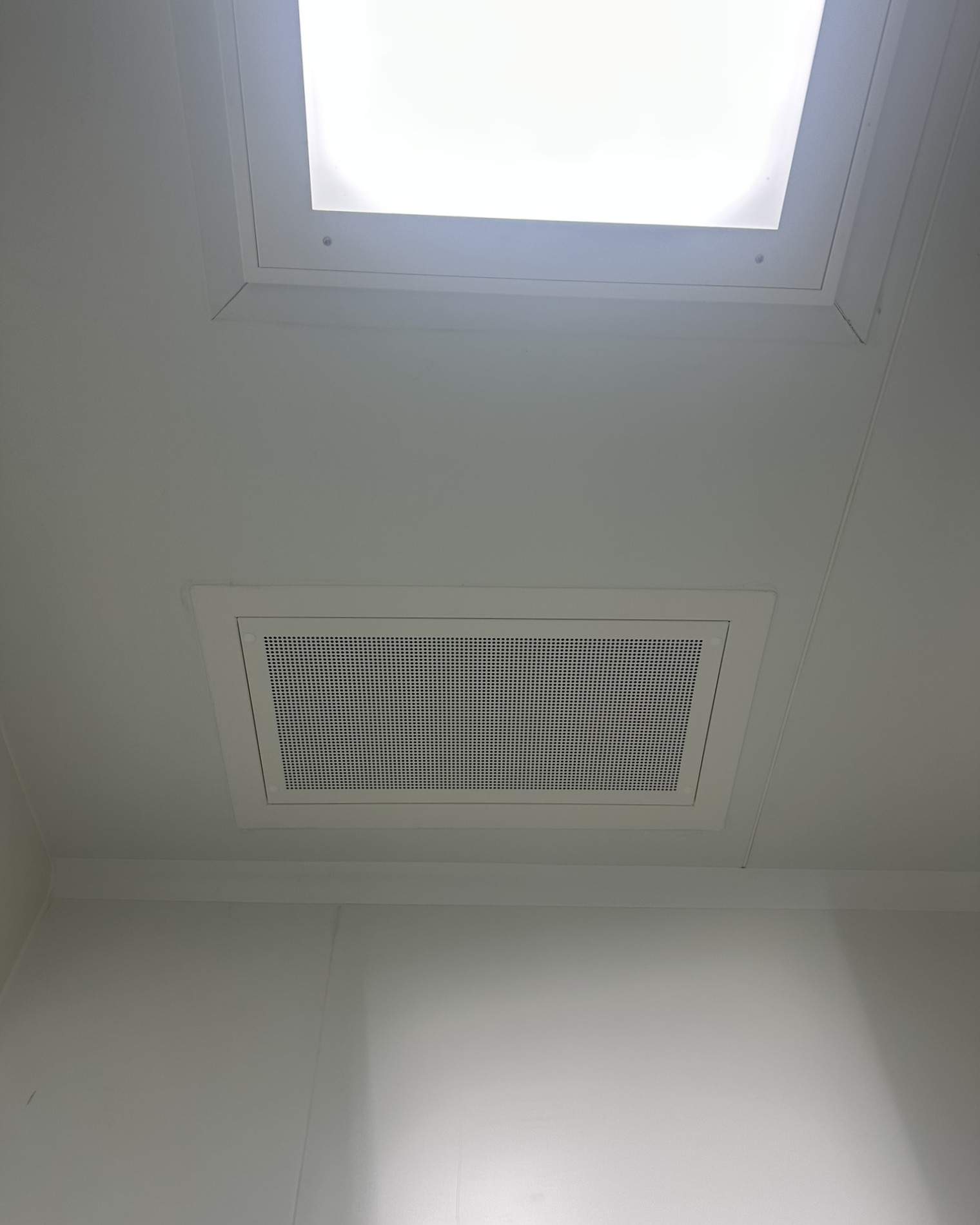 Diffuseur d'air plafonnier installé à côté d'un panneau lumineux dans une salle propre